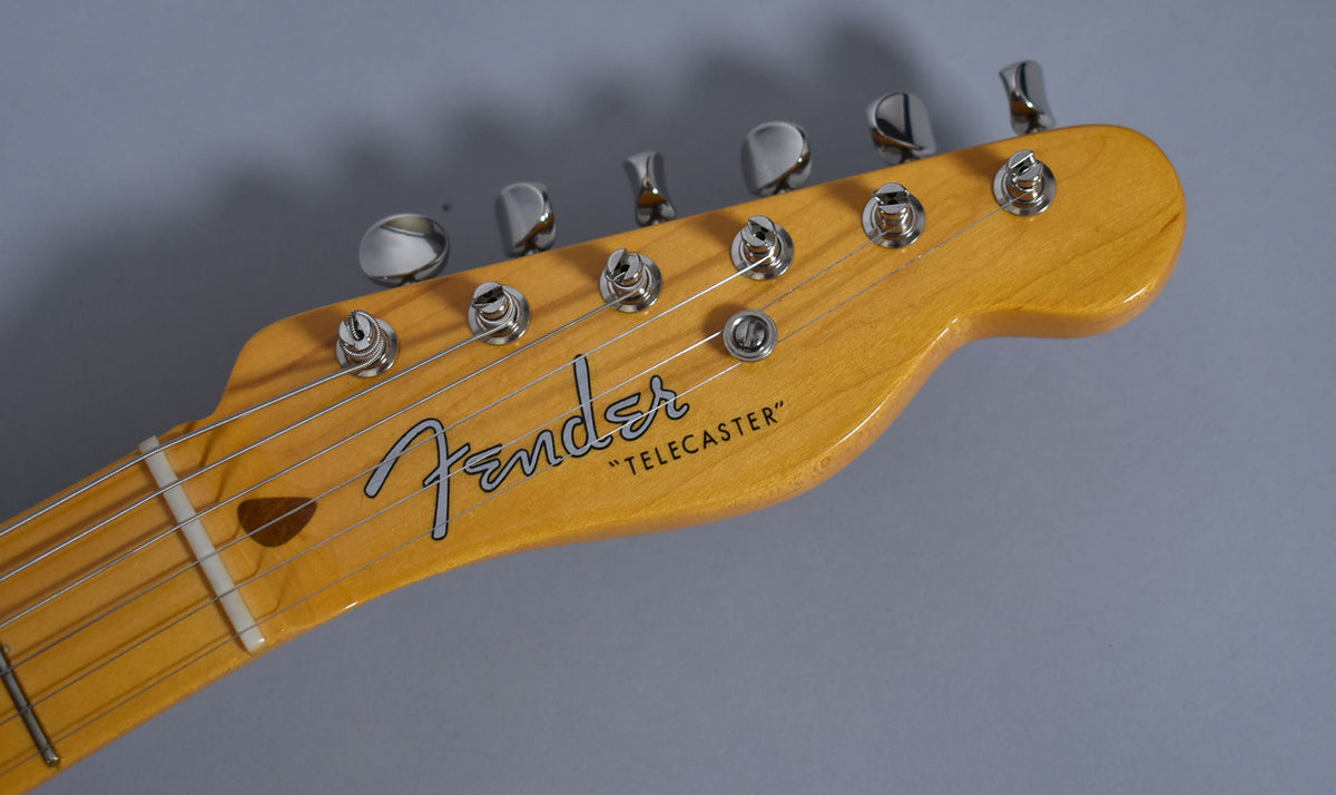Close-up of the Telecaster's headstock, angled from the left, showing the light maple finish, six chrome tuners, and string tree.