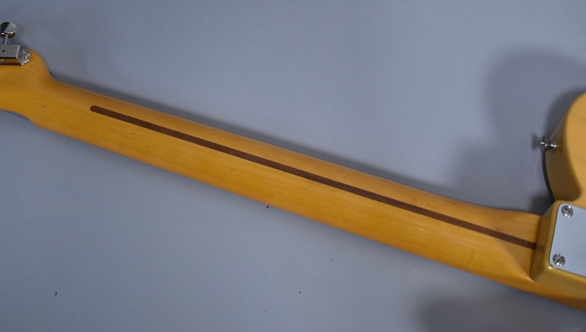 The guitar's light blonde neck, with a dark wood skunk stripe, is viewed from behind, showing the heel and a chrome tuning peg.