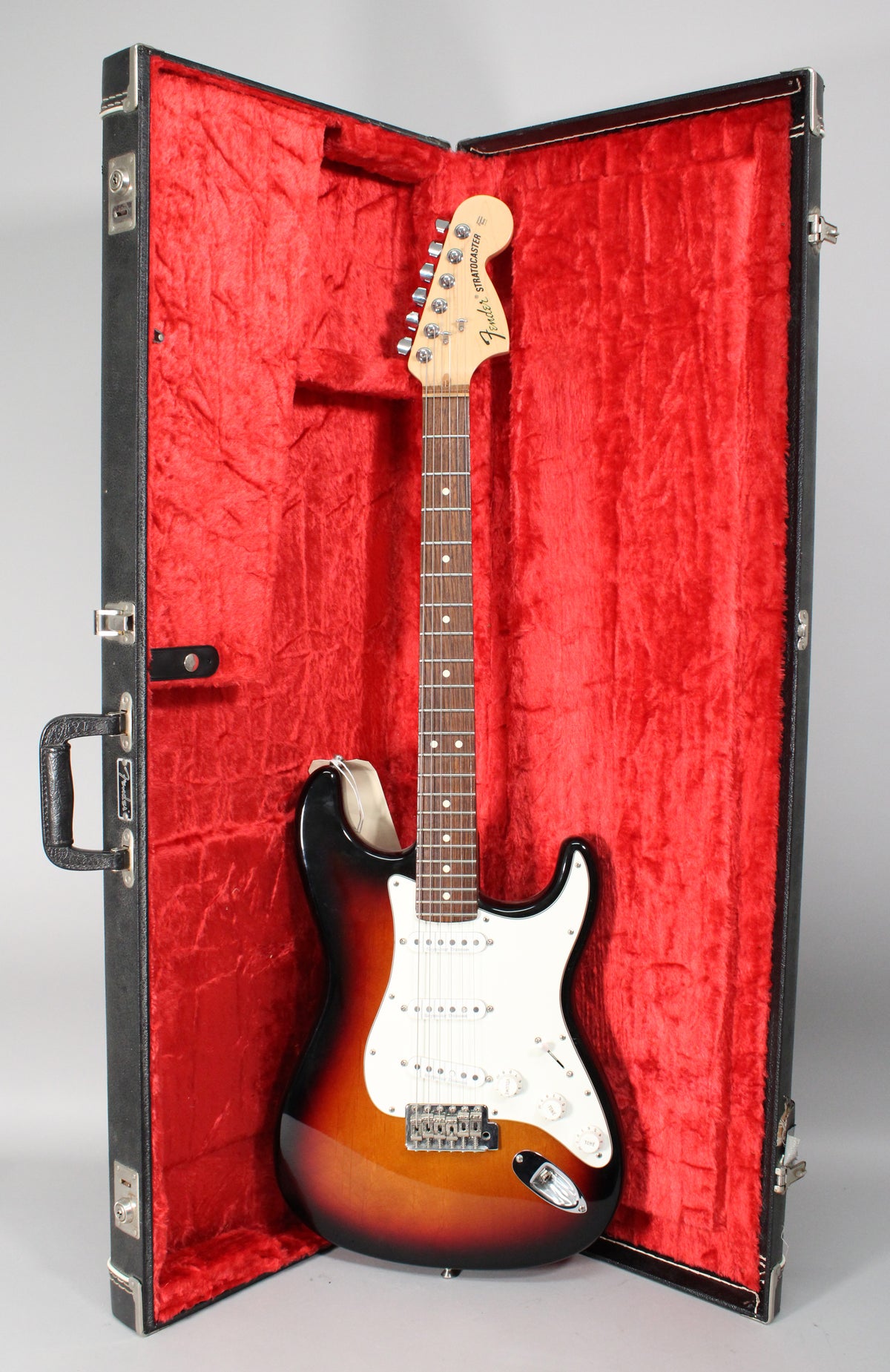 Full-length view of a sunburst electric guitar with a white pickguard, chrome hardware, and a maple neck, resting in a red-lined hard case.