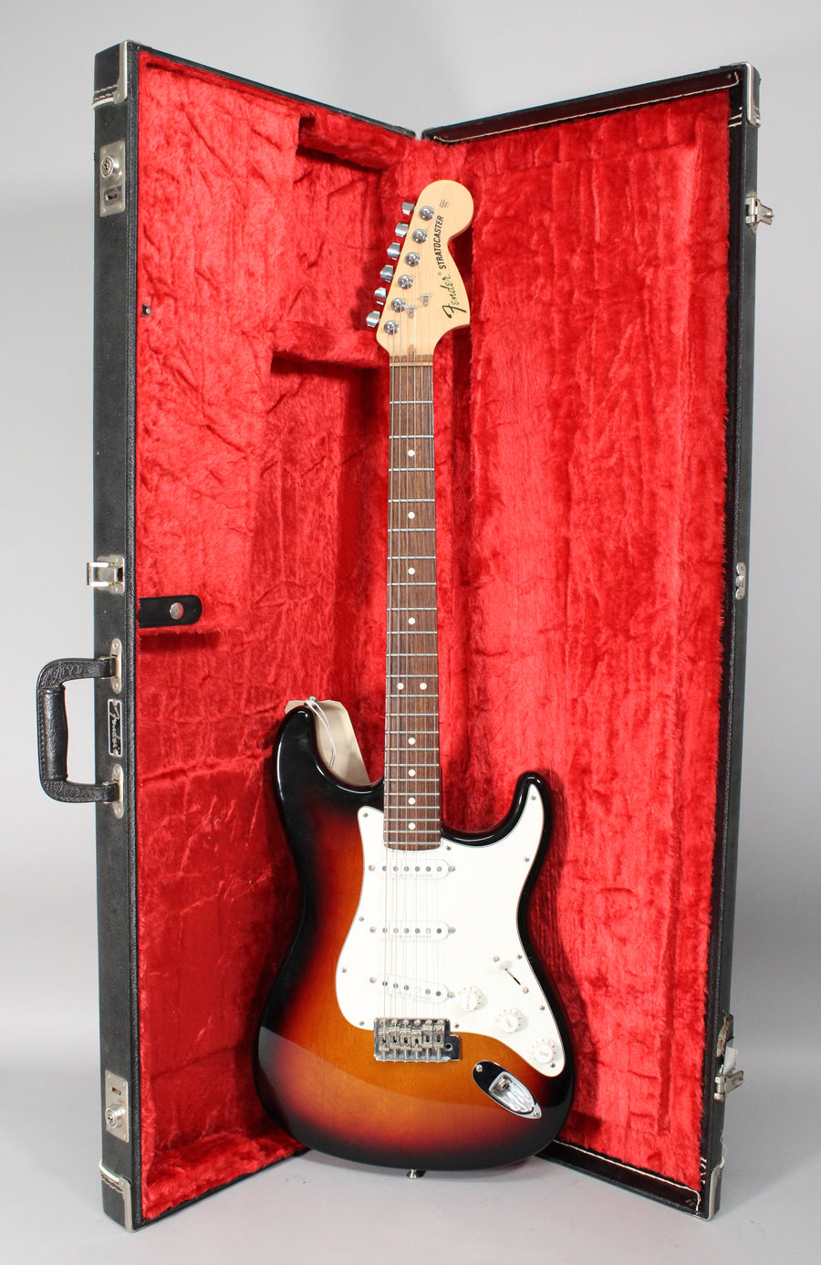 Full-length view of a sunburst electric guitar with a white pickguard, chrome hardware, and a maple neck, resting in a red-lined hard case.