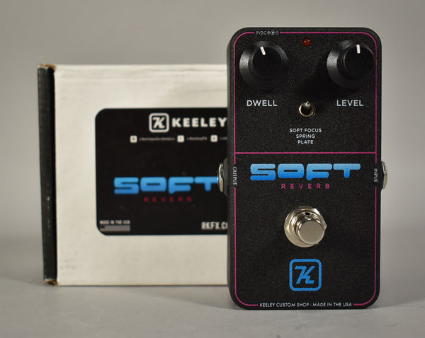 A black textured pedal with pink trim, two black knobs, a toggle switch, and a silver footswitch, shown with its box.