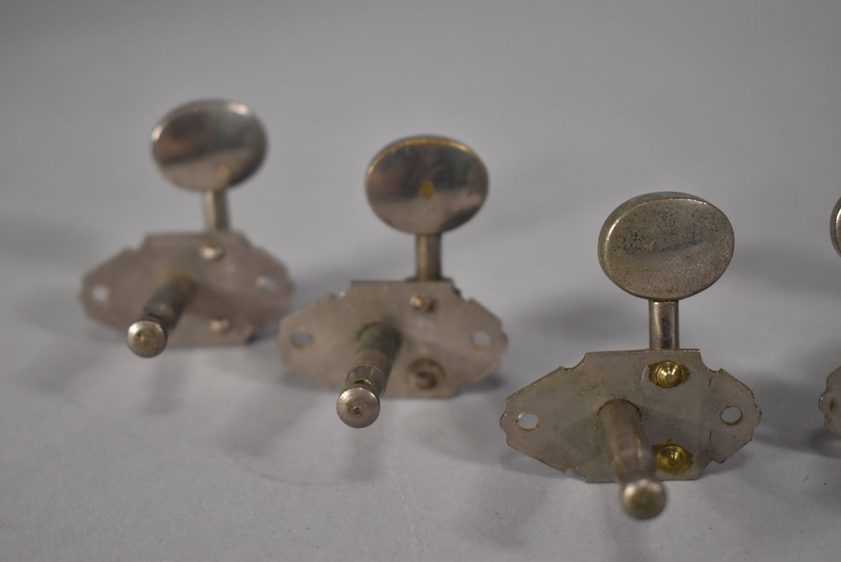 Three tarnished nickel tuners with oval buttons are shown from a low angle, revealing mounting plates and brass screws.