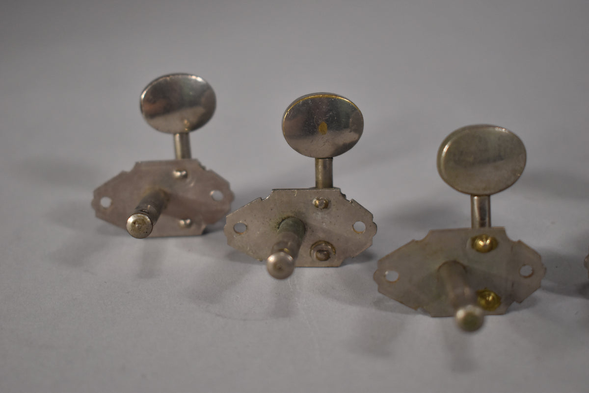 Three tarnished nickel tuners with oval buttons are shown from a low angle, revealing mounting screws and some green corrosion.