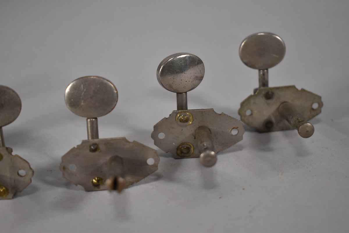 Three tarnished nickel tuners with oval buttons are angled, showing their mounting plates with brass screws and exposed gears.