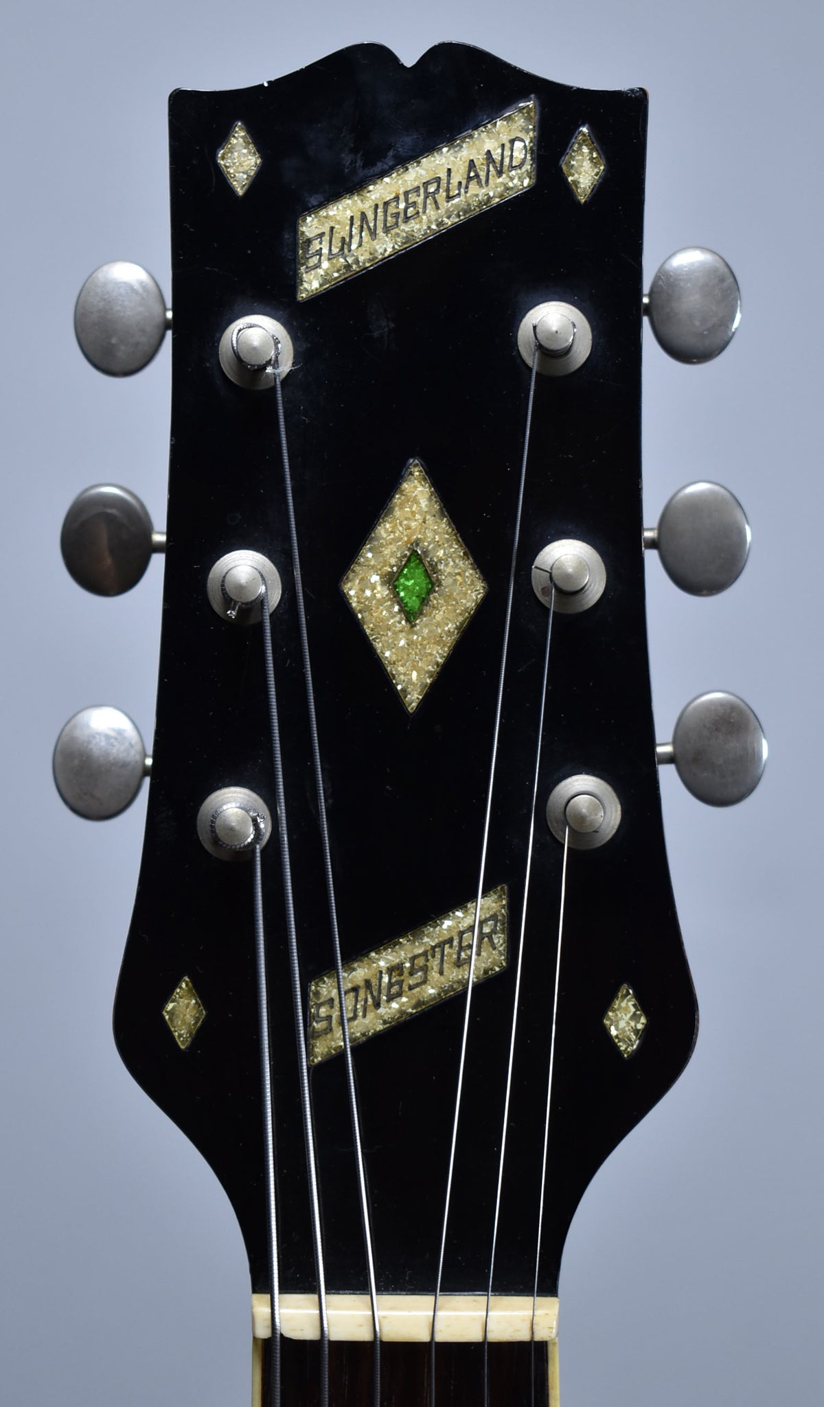 Close-up of the black headstock with six metal tuners, a large gold glitter diamond with a green center, and two gold glitter banners.