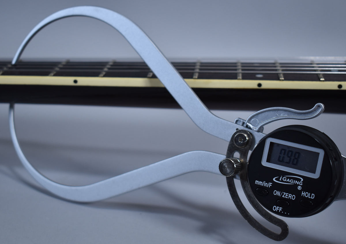 A digital caliper measures the dark brown fretboard and neck, showing a reading of 0.98.
