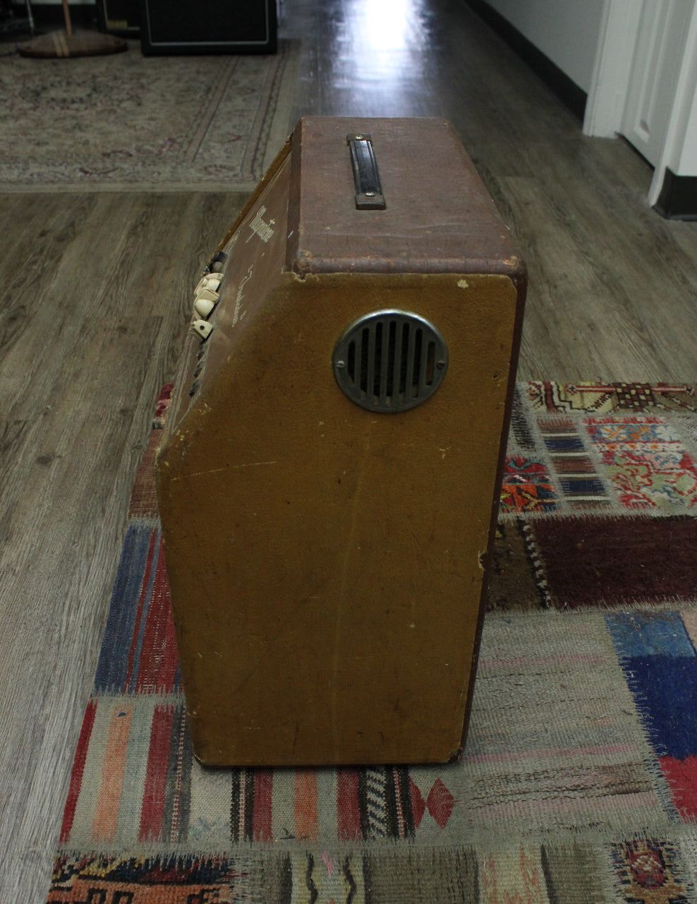 The brown combo amp is angled, showing its right side with a round metal vent, top handle, and some wear on the edges.