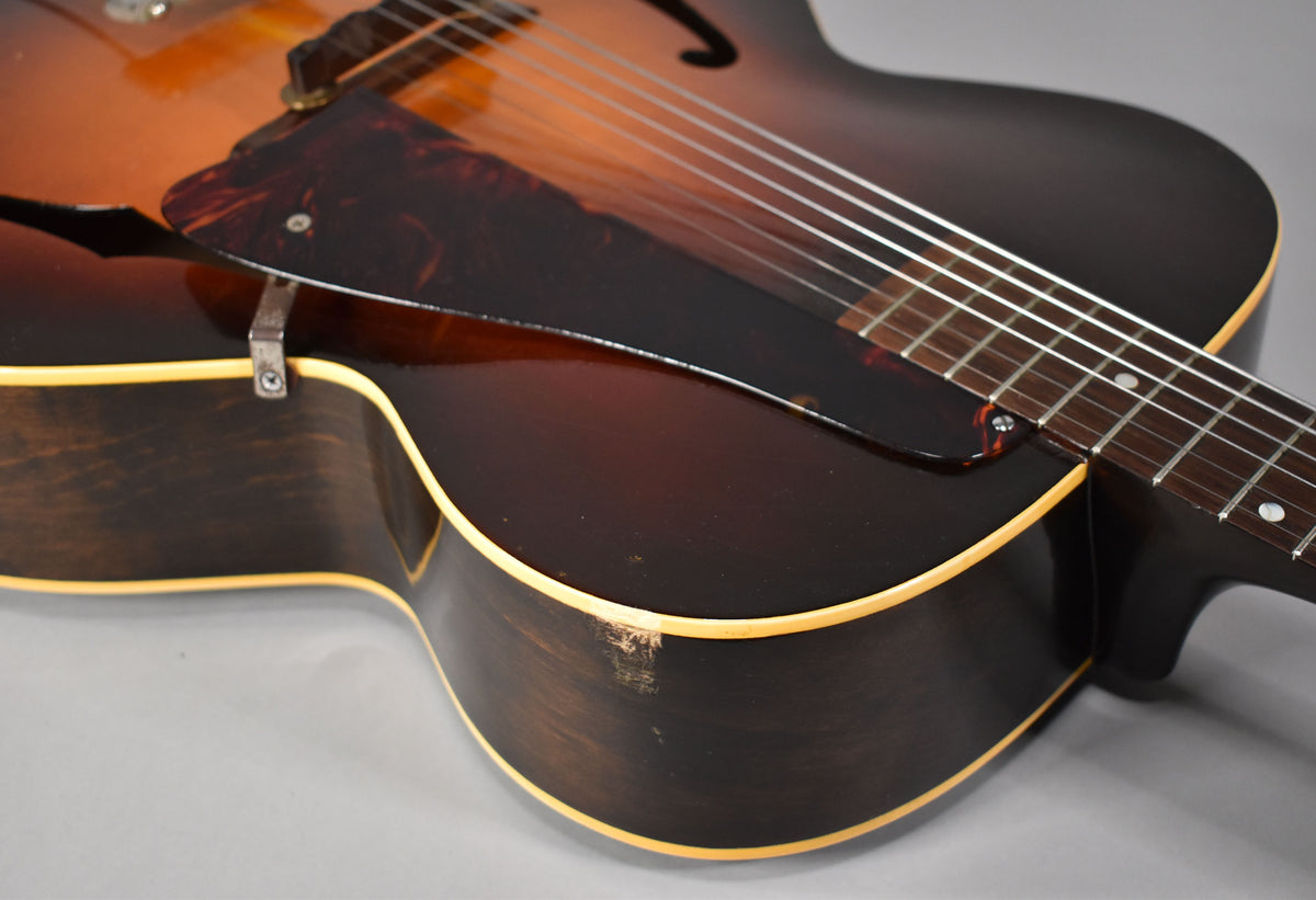 Close-up of the guitar's lower bout, showing the dark sunburst finish, tortoiseshell pickguard, and a chip in the binding on the side.