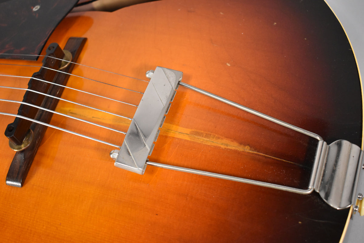 Close-up of the sunburst body, showing the chrome trapeze tailpiece, wooden bridge, and significant wear below the strings.