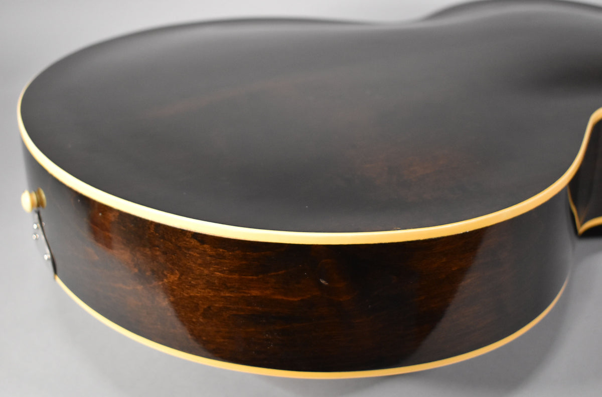 Close-up of the guitar's lower bout, showing the dark sunburst finish, cream binding, and a strap button on the lower side.