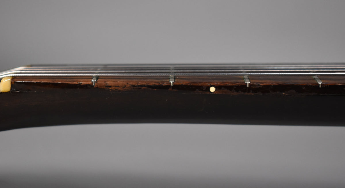 Close-up of the dark brown fretboard and neck, showing a cream nut, metal frets, and a single cream dot inlay.
