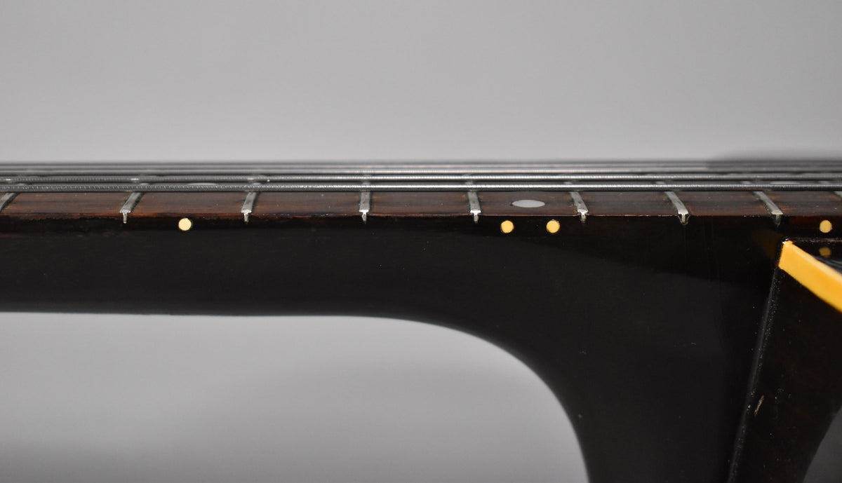 Close-up of a guitar fretboard with strings, frets, and side dot markers, showing the neck joint.