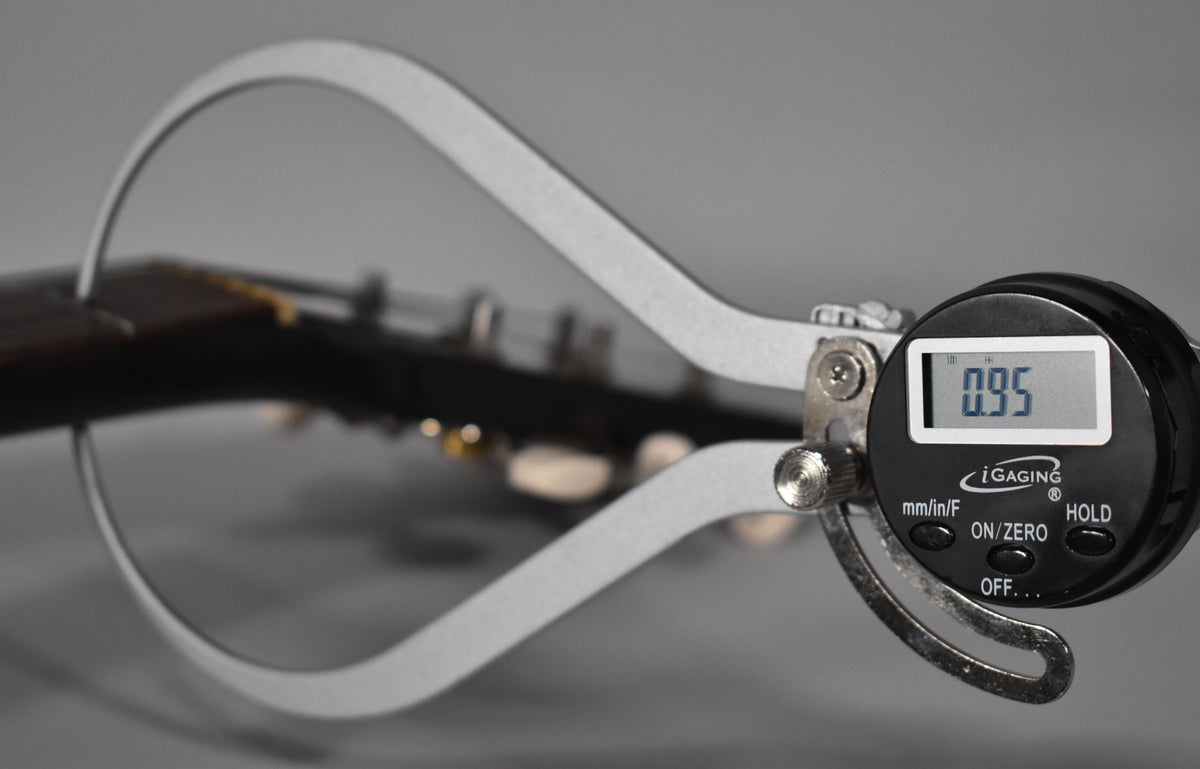 A digital caliper measures the guitar's nut width at 0.95 inches, with the dark headstock and tuning pegs blurred in the background.