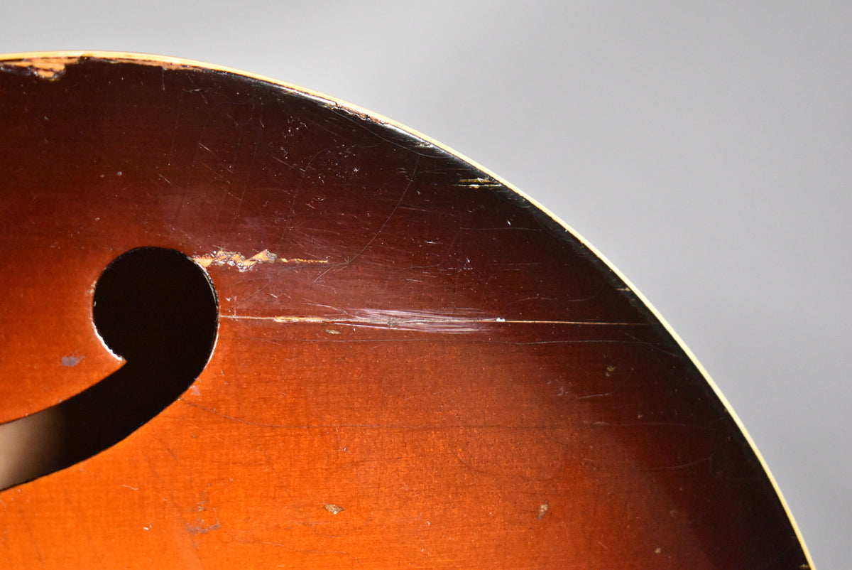 Close-up of the sunburst body, showing the upper curve of an f-hole and heavy wear, scratches, and finish loss on the dark brown top.