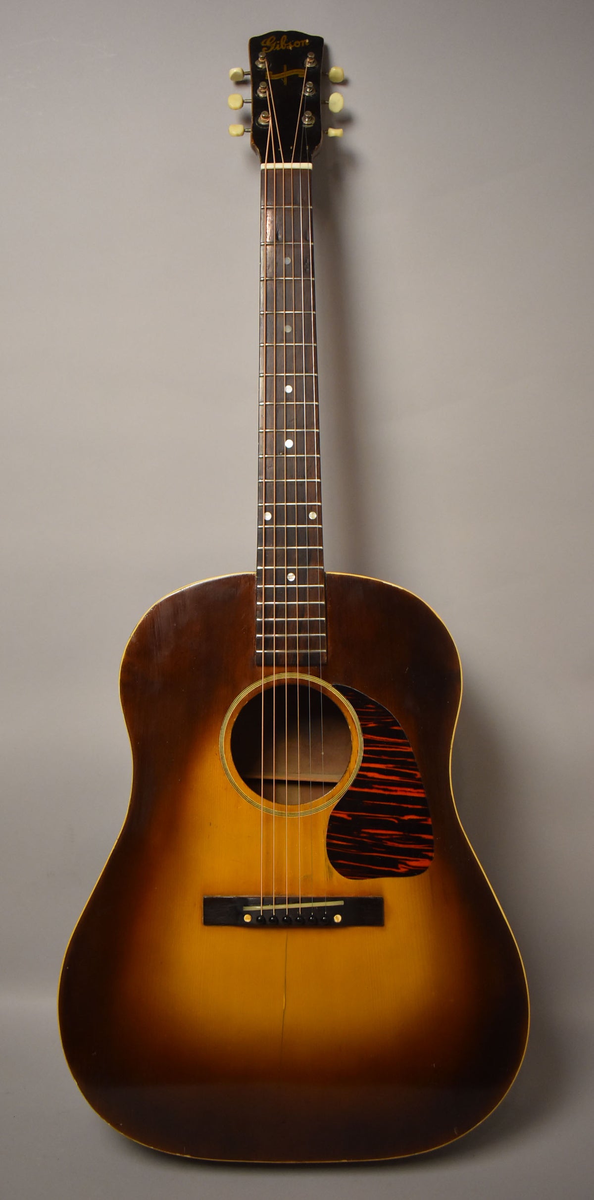 Full-front view of a sunburst acoustic guitar with a dark tortoiseshell pickguard, showing light wear and checking on the body.