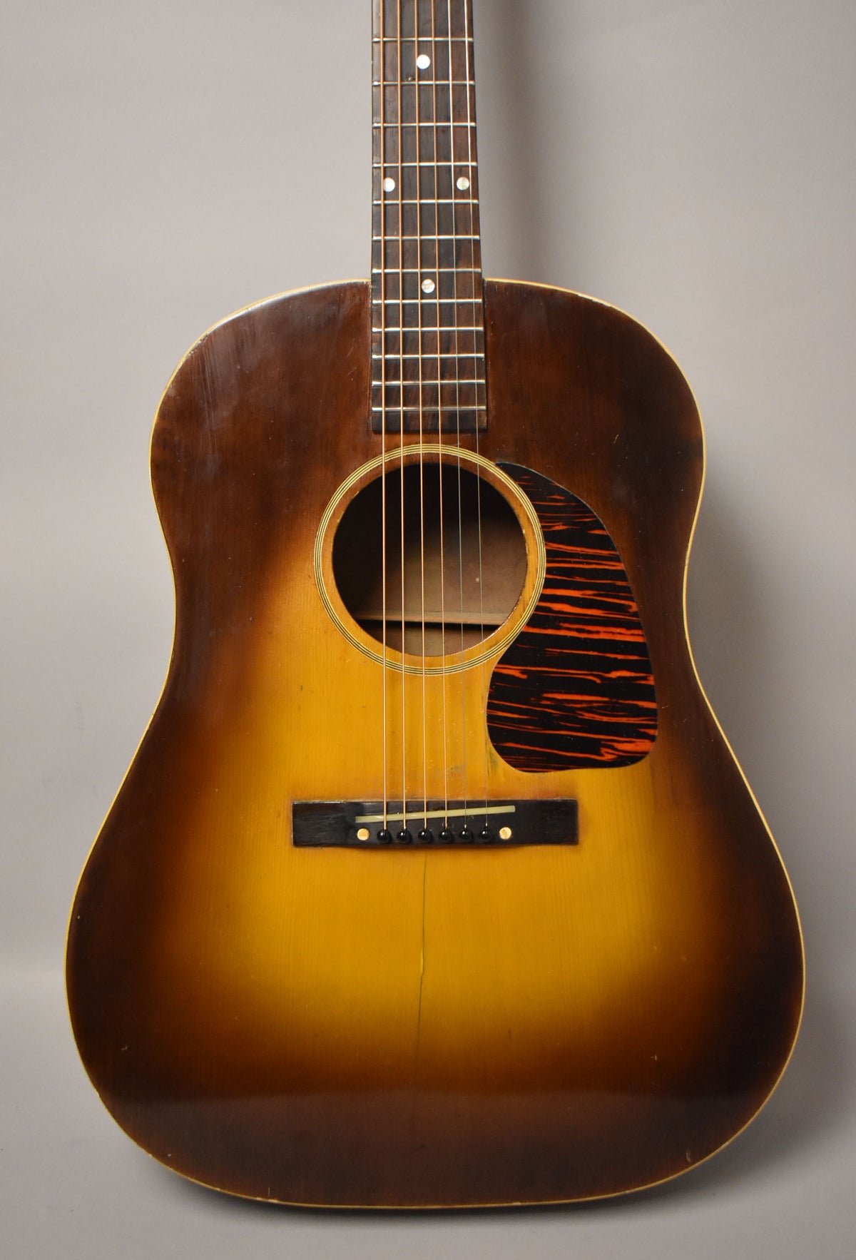 Full front view of a sunburst acoustic guitar with a dark tortoiseshell pickguard, showing finish wear and a visible crack below the bridge.