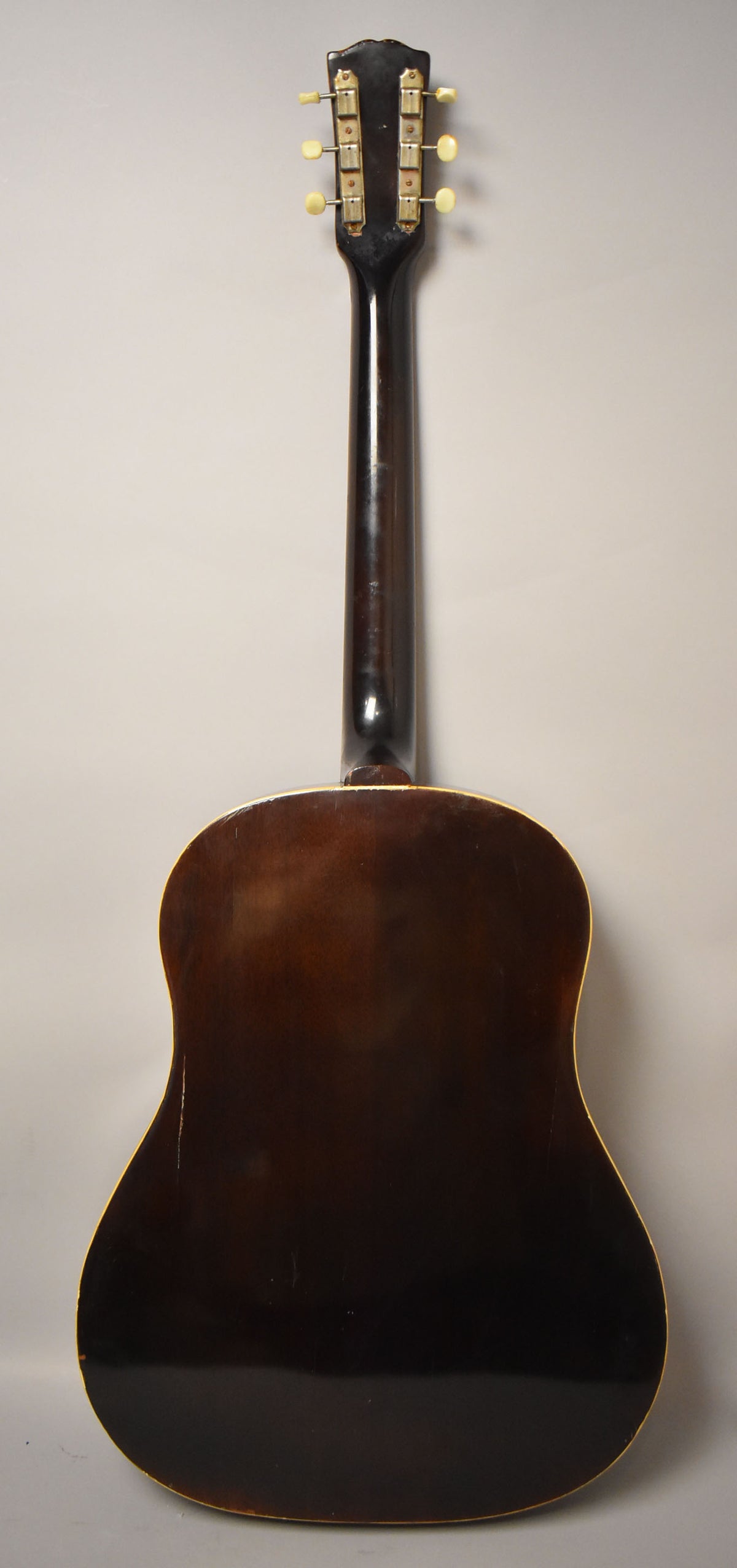 Full rear view of the dark sunburst acoustic guitar, showing the headstock with six cream tuners and the body with binding wear.
