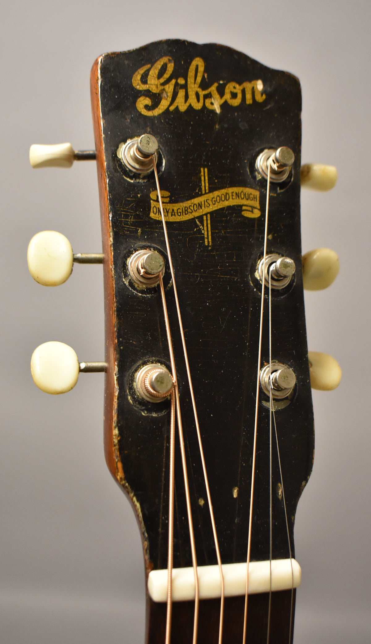 Close-up of the guitar's black headstock, showing six cream tuning pegs, a banner logo, and significant finish wear and checking.