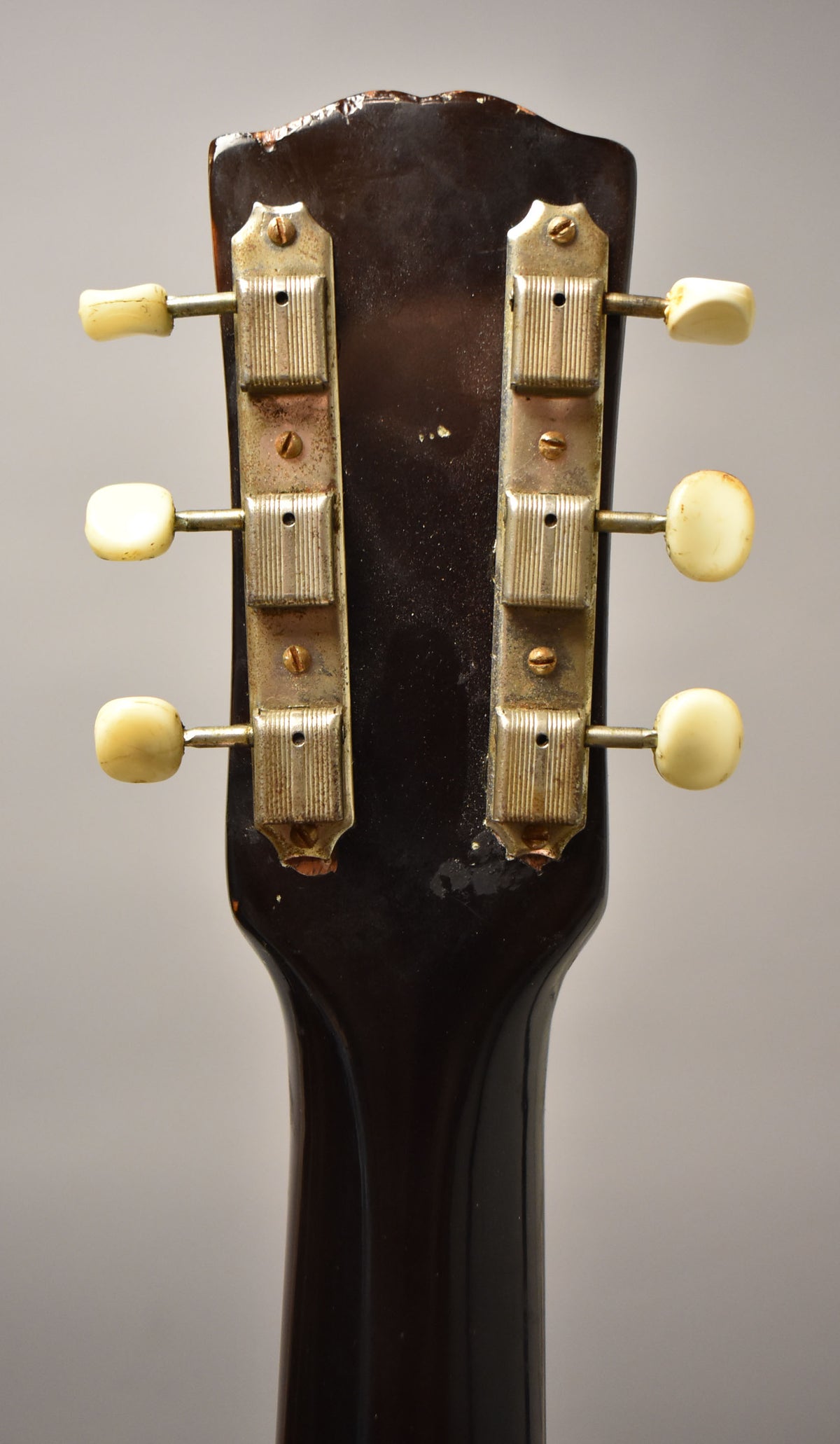 Rear view of the dark brown headstock and upper neck, showing six cream tuning pegs on tarnished metal strips.