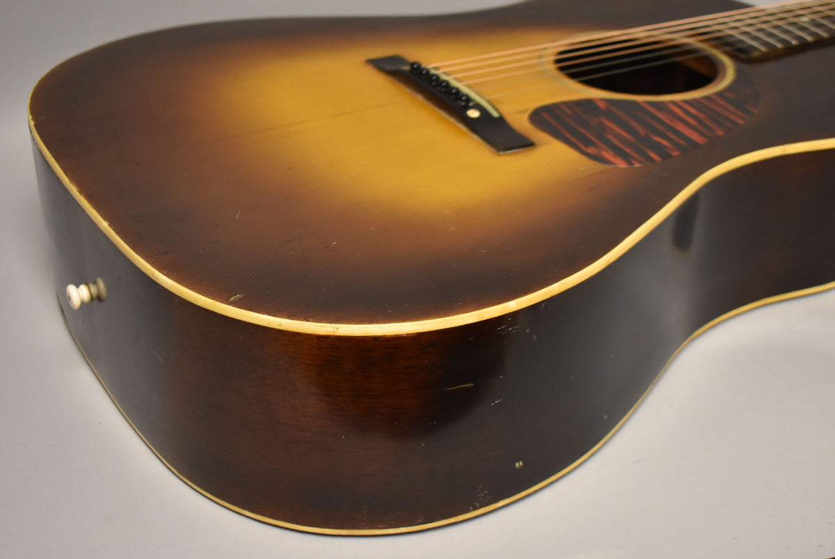 The lower bout of a sunburst acoustic guitar, showing the dark brown sides, cream binding, and a few small dings.