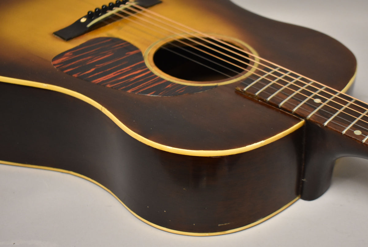 Close-up of the sunburst acoustic guitar's lower bout and fretboard, showing a dark brown finish with light binding and some wear.