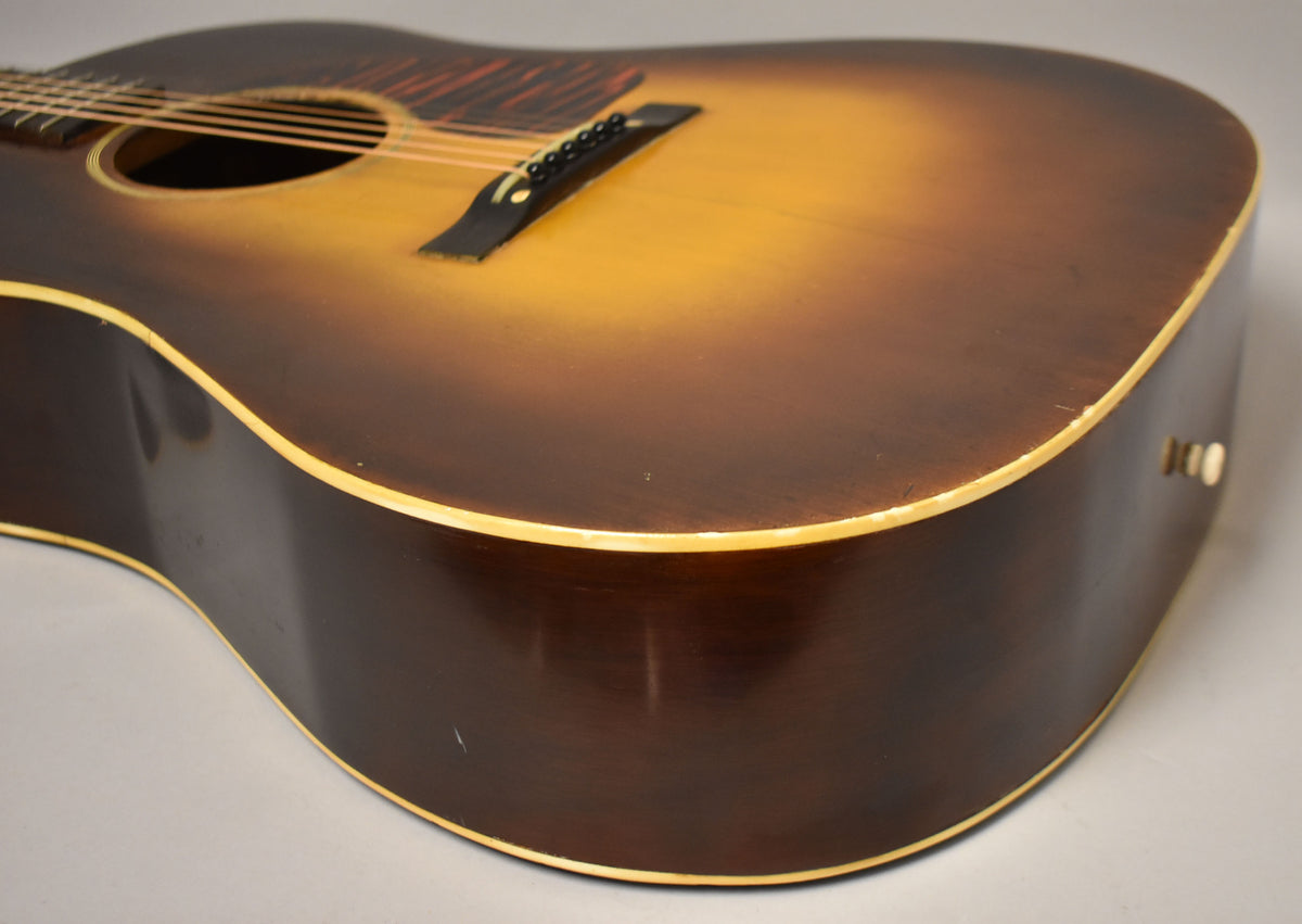 The lower bout of a sunburst acoustic guitar, showing the dark brown sides, light binding, and some finish wear.