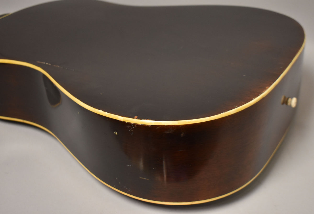 The dark sunburst acoustic guitar's lower bout and side show finish wear, binding discoloration, and a visible endpin jack.