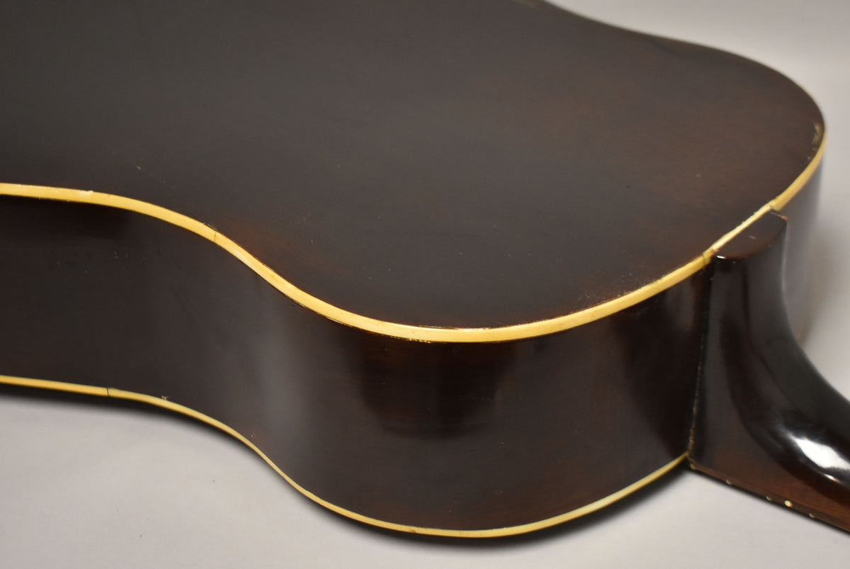 Close-up of the guitar's dark brown back and side, showing cream binding and some finish wear along the edges and neck heel.
