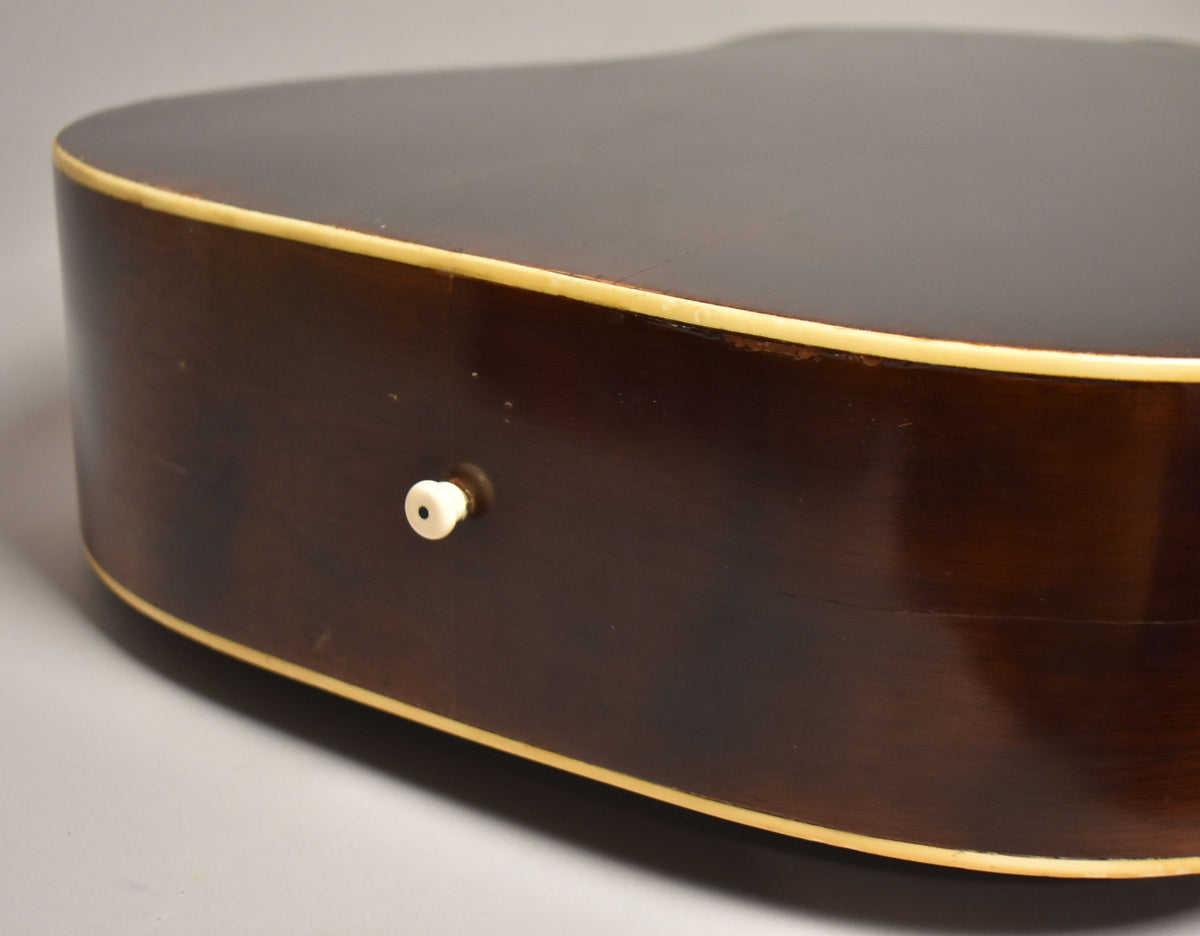 Close-up of the guitar's dark brown side, showing a cream binding, a white endpin, and some finish wear near the upper binding.