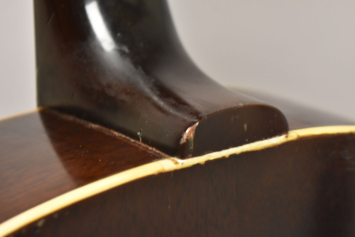 Close-up of the guitar's dark brown neck heel and body binding, showing finish wear and chipping where the neck meets the body.