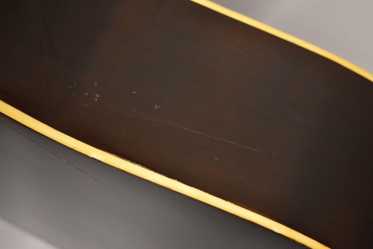 Close-up of the guitar's dark brown body with a yellow binding, showing light scratches and small white flecks on the surface.