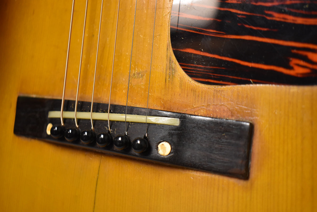 Close-up of the guitar's sunburst body, showing the dark bridge with six black pins, a light saddle, and a tortoiseshell pickguard.