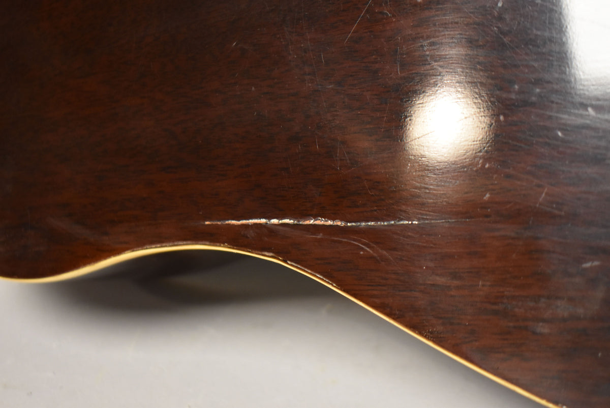 Close-up of the guitar's dark brown body, showing a long, horizontal scratch with exposed wood and lighter binding along the bottom curve.