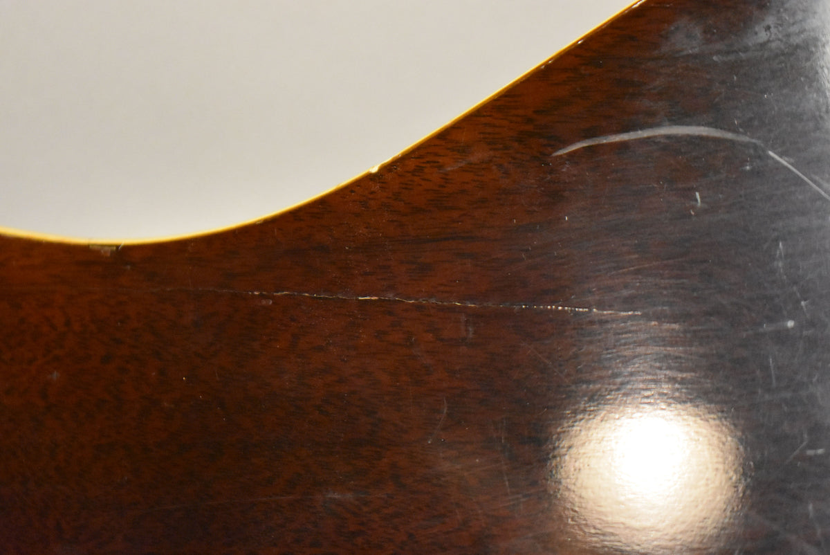Close-up of the dark brown body with a long horizontal crack, many scratches, and a bright light reflection on the lower right.
