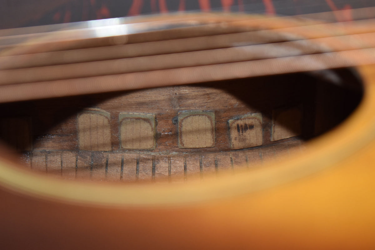 Close-up inside the soundhole shows the worn wooden bridge plate and bracing, with some dark marks on the far right brace.
