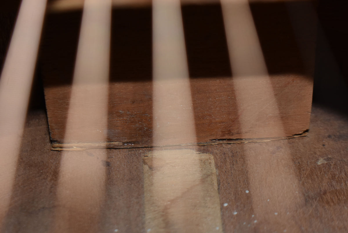 Close-up inside the guitar body, showing the neck block and bracing, with light stripes from the soundhole.