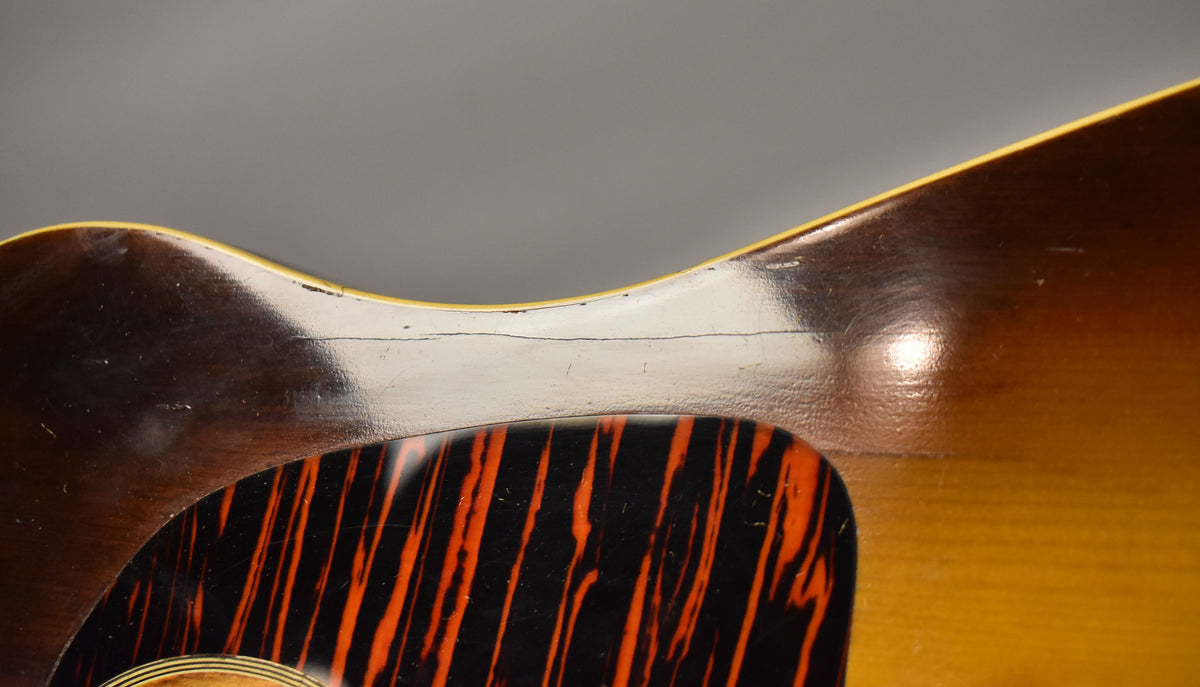 Close-up of the guitar's upper bout, showing a dark sunburst finish with a visible crack across the top and an orange-striped pickguard.
