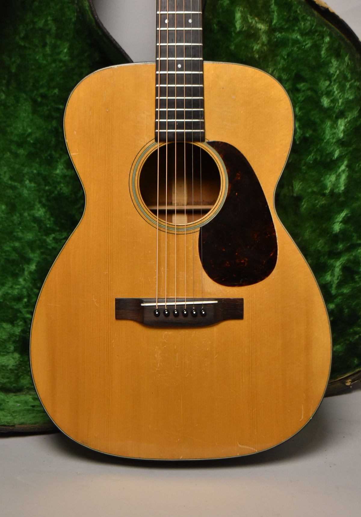 Full front view of a natural finish acoustic guitar with a dark pickguard, showing light wear and checking on the body.