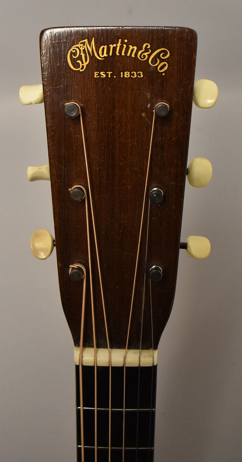 The dark brown headstock, with six cream tuning pegs, shows visible finish wear and checking, with a cream nut and dark fretboard.