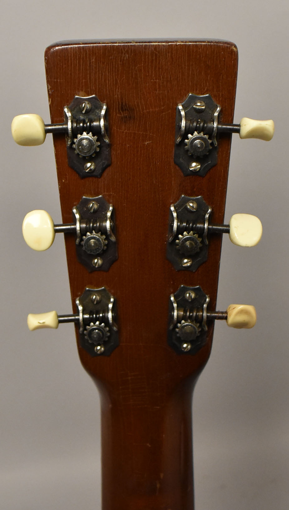 The guitar's dark brown headstock, viewed from behind, shows six cream-colored tuning pegs and visible finish checking.