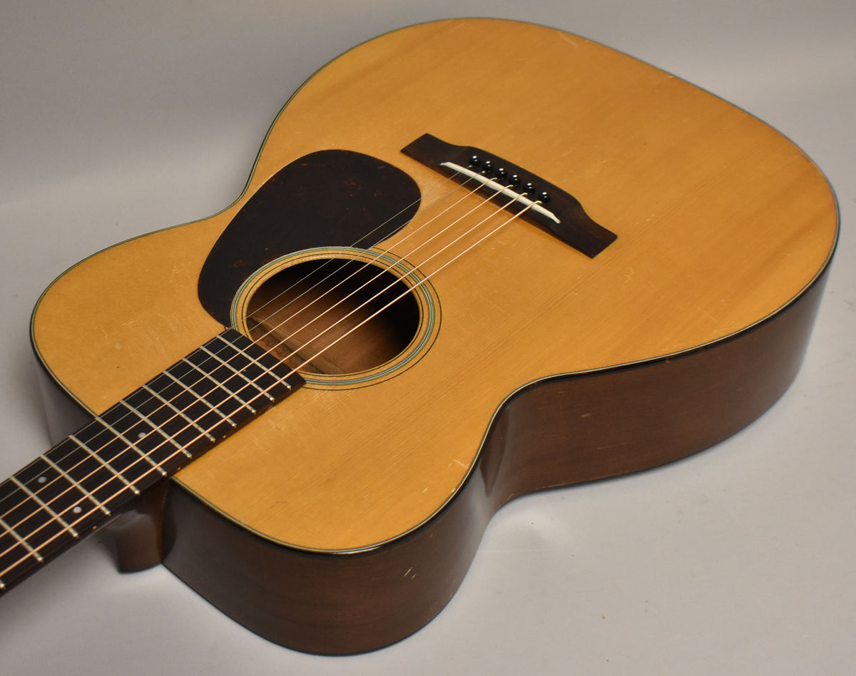 The natural finish acoustic guitar is angled right, showing the light top, dark sides, black pickguard, and fretboard with dot inlays.