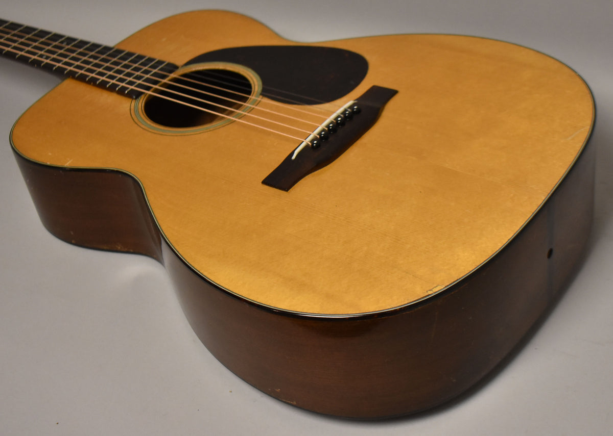 The natural finish acoustic guitar is angled from the upper left, showing its light top, dark sides, black pickguard, and bridge.