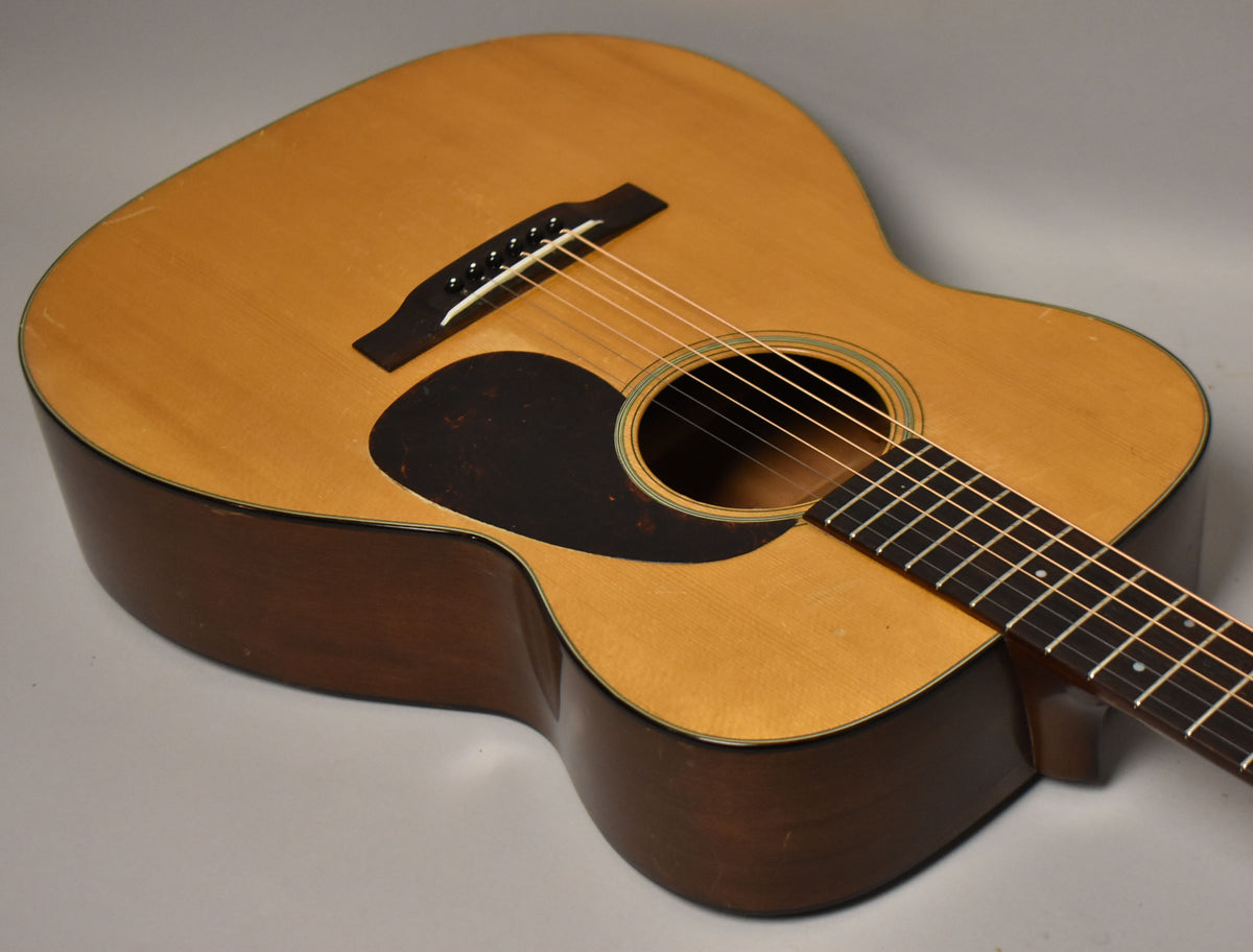 The acoustic guitar's light natural top and dark sides are angled, showing the pickguard, bridge, soundhole, and fretboard with wear.