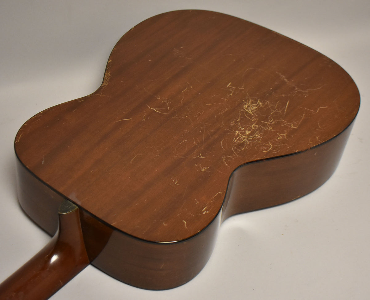 The acoustic guitar's dark brown back and sides show extensive finish checking and wear, with the neck visible at the lower left.