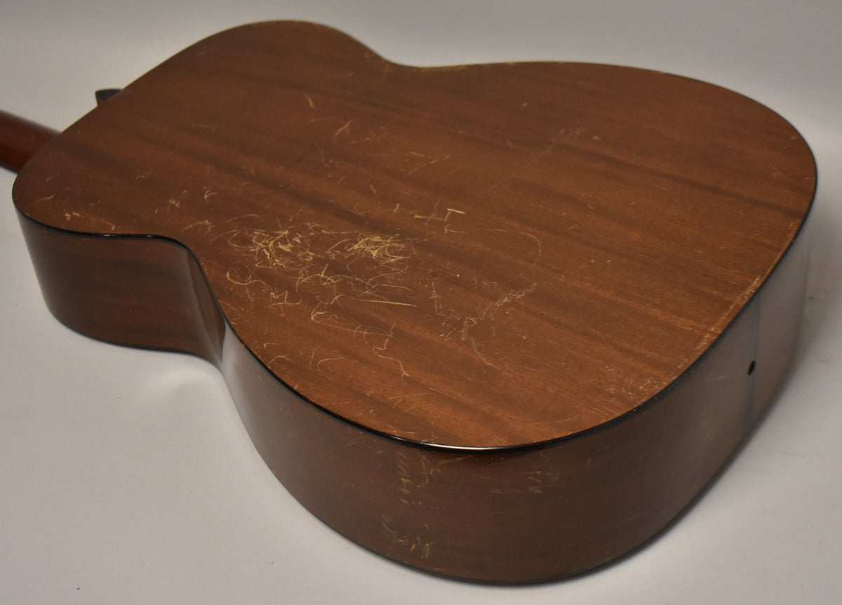 The dark brown acoustic guitar's back and side are visible, showing extensive finish checking and scratches across the surface.