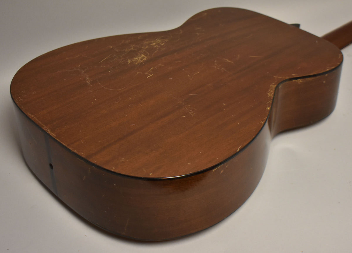 The guitar's natural finish back and sides are visible, showing extensive wear, scratches, and finish checking across the surface.