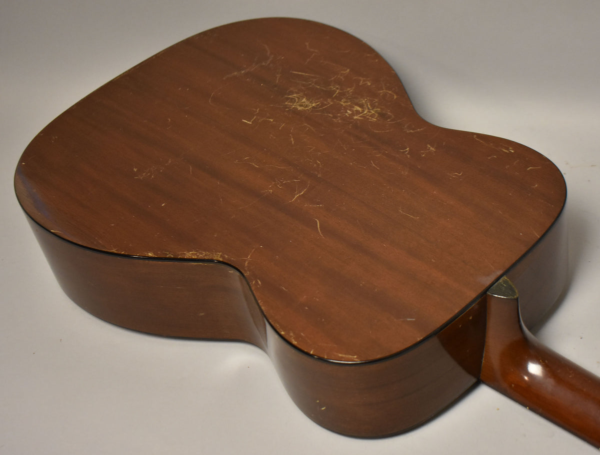 The guitar's dark brown back and side are angled, showing heavy finish wear, scratches, and some flaking, with the neck heel visible.