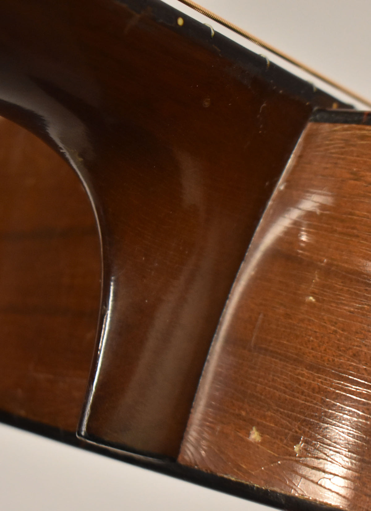 Close-up of the guitar's dark brown neck heel and lower bout, showing finish checking, scratches, and small chips on the body.