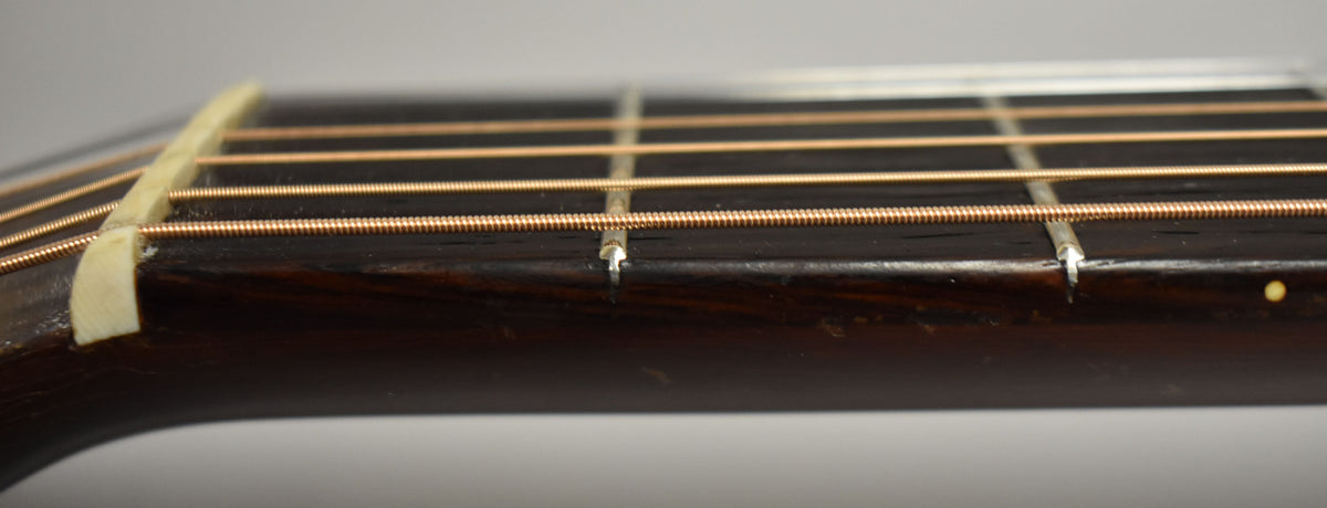 Close-up of the dark fretboard and bronze strings, showing the bone nut and first few frets with some wear and a side dot.