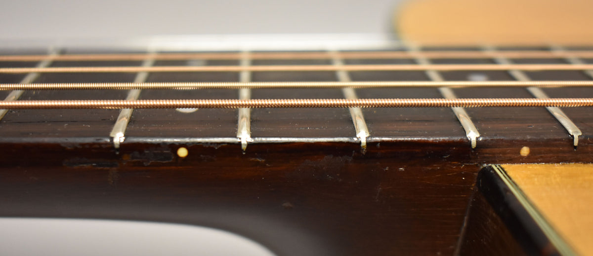 Close-up of the dark fretboard and bronze strings, showing wear on the lower edge and a small dot inlay.
